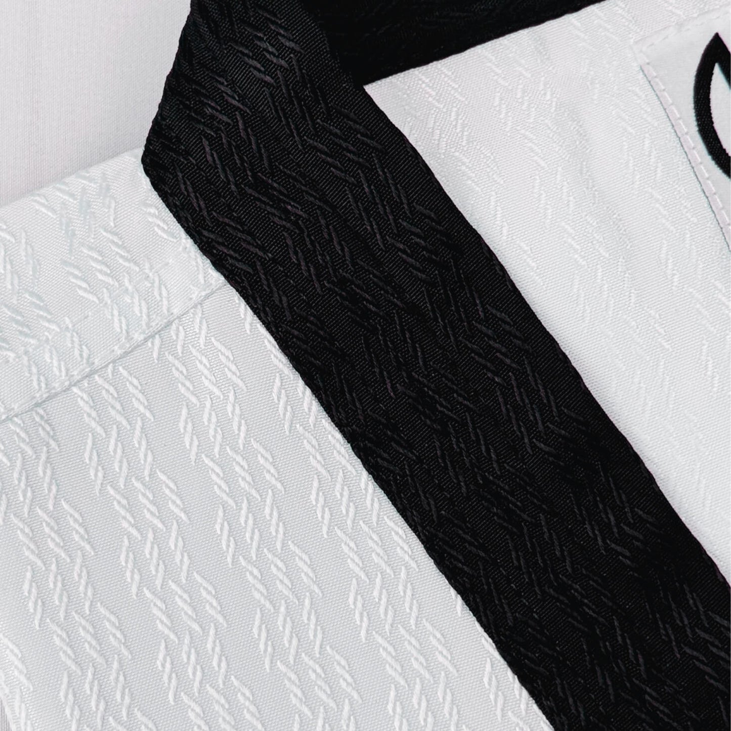 Close-up of a white martial arts uniform with a black belt on a light gray background- breathable and durable for high performance.